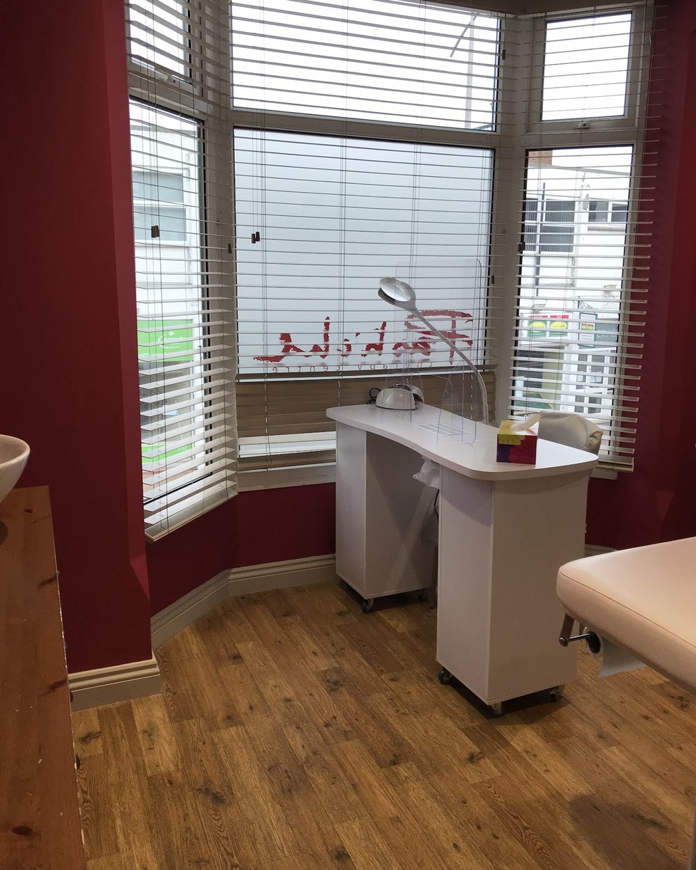 The nail room in the bay window at the front, with the Pastiche name painted on the glass and a white manicure desk under the blinds