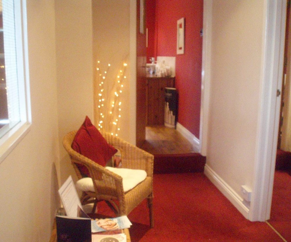 The hallway inside the front door, with a wicker chair, fairy lights and a red carpet running back towards the treatment rooms