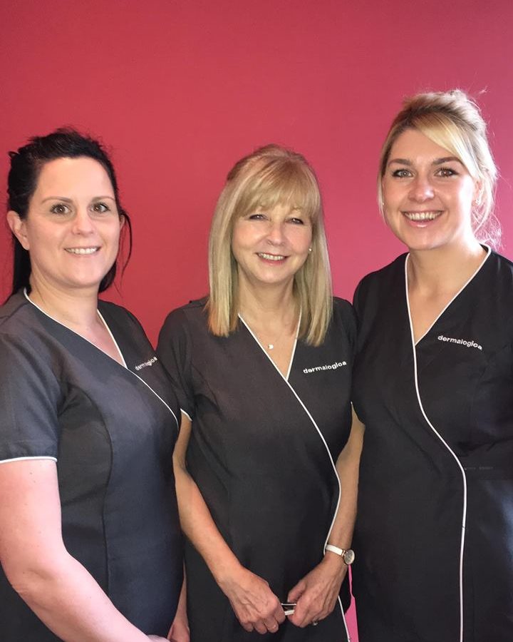 Three of the Pastiche therapists in black tunics, standing together against a pink wall in the salon